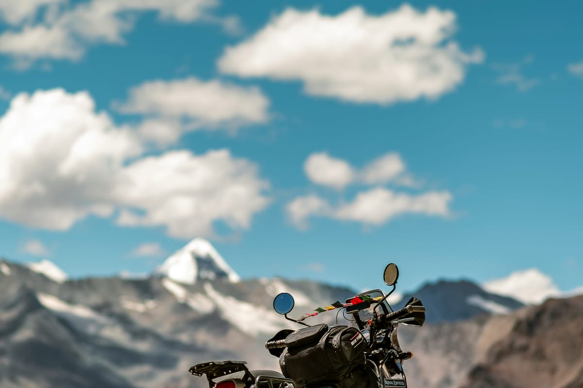 Royal Enfield parked on a Ladakh highway with snow-capped peaks behind, renting a bike is one of the best-value and most iconic transport choices
